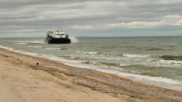Coast Guard hovercraft moving along the beach. Patrolling the coastline. Overcast skies, muddy sea. Side view from the front. Slow motion