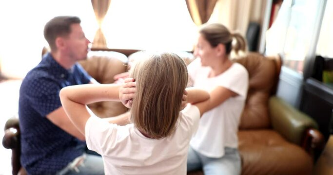 Teen girl covers ears with hands to avoid listening to argument of parents. Man and woman sit on sofa quarreling in presence of daughter slow motion
