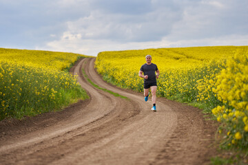 Obraz premium Distance runner running on a road through canola field