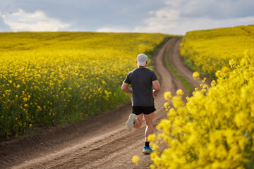 Distance runner running on a road through canola field