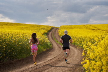 Fototapeta premium Endurance runners on a dirt track in a canola field, training