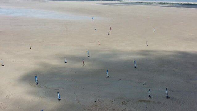 Blokarts or landyachts race across dry landscape with cloud shadows on ground, aerial