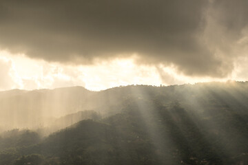 Early morning landscape. Hill view with rain shower during sunrise. View from above. Rays of the sun breaking through the rain among the hills.