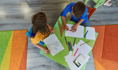 Cute girl and boy sit and draw together in preschool institution
