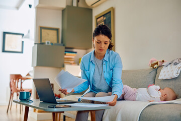 Stay at home mother analyzing paperwork while working from home.