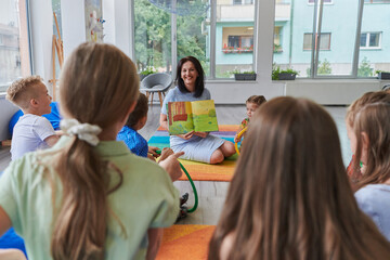Reading time in an elementary school or kindergarten, a teacher reading a book to children in an...