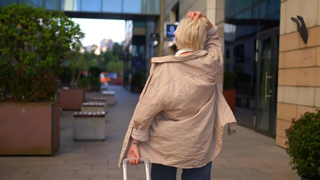 a positive and cheerful young woman traveler on the street with a suitcase in her hands turns around and smiles at the camera