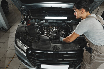 Young male mechanic examining engine under hood of car at the repair garage