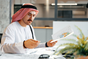 Young muslim businessman in traditional outfit working at the table in office