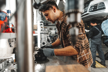 Fototapeta na wymiar Young man mechanic repairing car parts on worktable in car service shop