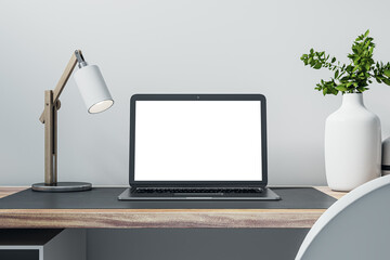 Closeup front view of home workplace with wooden desk with blank screen modern laptop, lamp and plant on light wall background in cozy interior, mockup. Remote work concept. 3D Rendering