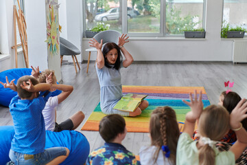 A happy female teacher sitting and playing hand games with a group of little schoolchildren