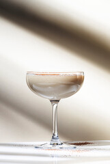 Brandy alexander alcoholic cocktail with cognac, cocoa liquor, cream, grated nutmeg and ice. Light beige background, hard light, shadow pattern. Minimalism