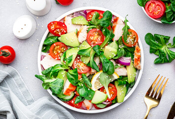 Chicken and vegetables salad with tomatoes,  avocado, cucumber, onion, lamb lettuce and sesame seeds on gray table background, top view