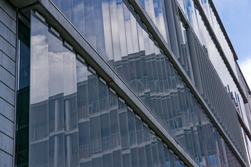 Fototapeta na wymiar Close-up of modern facade of office building with reflections at City of Zürich district Oerlikon on a blue cloudy spring day. Photo taken May 12th, 2023, Zurich, Switzerland.