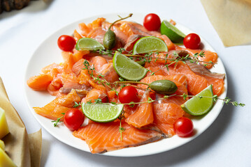 A colorful plate of smoked salmon with capers, red cherry tomatoes and a lime wedge, the perfect...