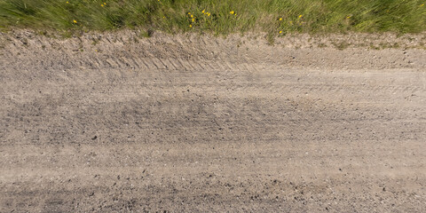 Fototapeta na wymiar panorama of surface from above of gravel road with car tire tracks with roadside and grass