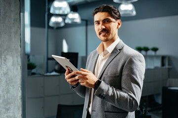 Fototapeta na wymiar Young successful businessman working on digital tablet while standing in office