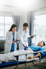 Obraz premium Two doctors talking to a patient lying in his bed with receiving saline solution in hospital .