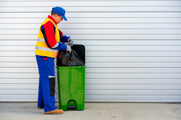 Janitor takes garbage out of trash container outdoors