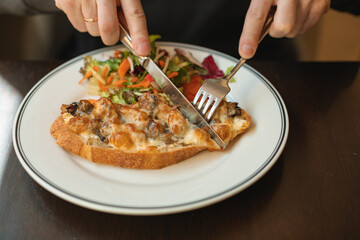 Close-up of a man eating a sandwich with bacon, cheese, mushrooms with a fork and knife.