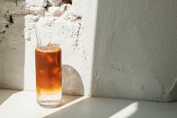 Coffee with tonic, lemon and ice cubes on white background with a sunbeam from the window. Summer...