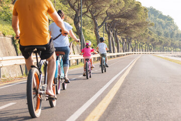 Family of four, parents with son and little daughter relaxed cycling on a coastal route, with a view out over the sea