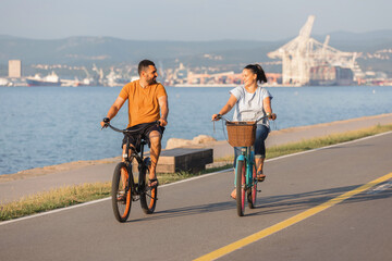 Fototapeta premium Couple taking pleasure in the ride on beach cruiser bikes, pedaling on a wonderful route near the sea