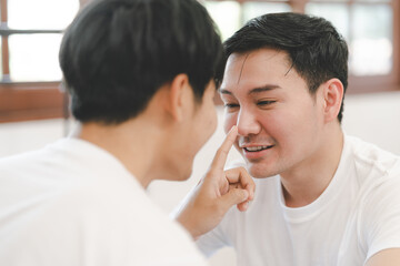 Asian gay couple touching boyfriend nose and smiling while resting at home. Cute gay couple playing in bed. LGBT lovers expressions of love concept