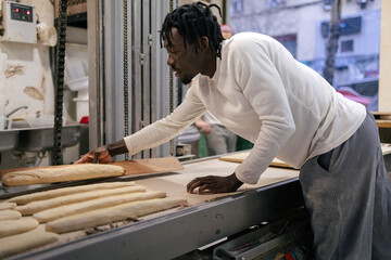 Young black baker placing bread on conveyor belt