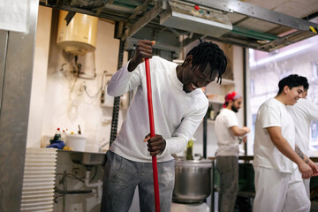 Young black baker cleaning with broom