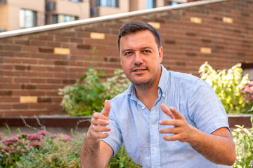 Positive talking mature man looking at camera, outdoors at recreational area. Male webcam recording interview. Millennial man sitting at park and having video conference call on laptop outdoors