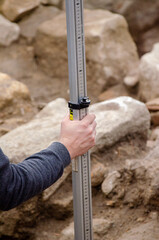 Worker holdings a telescopic leveling lath is helping surveyor, geodesist to measure position,...