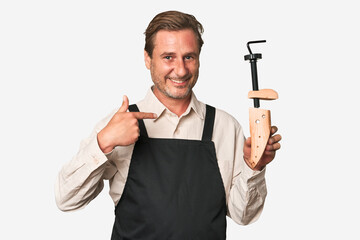 A middle-aged shoe maker person pointing by hand to a shirt copy space, proud and confident