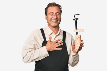 A middle-aged shoe maker laughs out loudly keeping hand on chest.