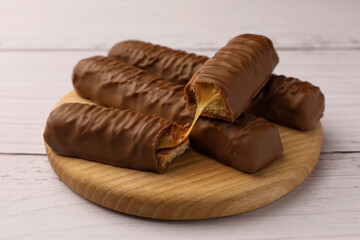 Tasty chocolate bars with caramel on white wooden table