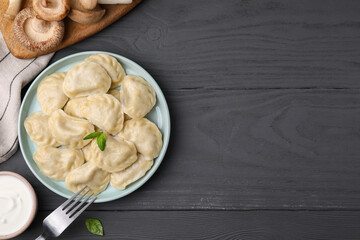 Plate of delicious dumplings (varenyky) with mushrooms on grey wooden table, flat lay. Space for...