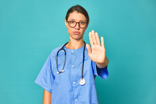 A young nurse woman isolated standing with outstretched hand showing stop sign, preventing you.