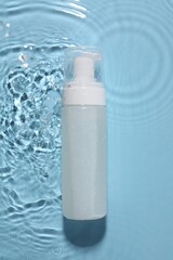 Bottle of face cleansing product in water against light blue background, top view