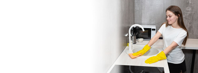 Banner with young girl cleaning the kitchen. Cleaning girl smiling and washes the sink with a napkin. Apartment, home cleaning service. Copy space. Place for text and your advertising.