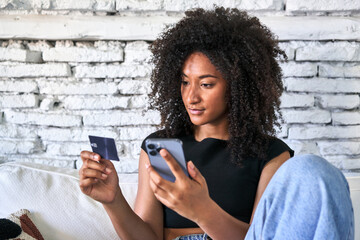 Relaxed afro-haired woman effortlessly shops online with credit card and phone at home.