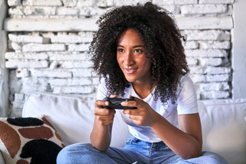 Joyful young woman plays video game on sofa, immersed in fun.