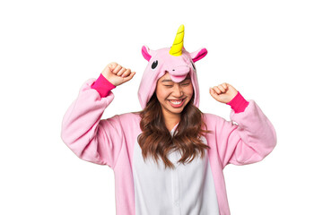 Vibrant young Asian woman leaps with joy in unicorn pajamas, creating a magical studio moment.