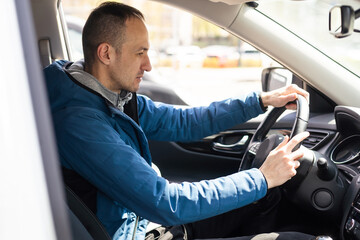 Handsome man in his 30s sitting in the driver's seat and smiling. Taxi driver listening to music on the car and changing the radio station.