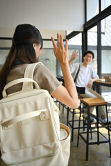 Cheerful asian man student waving hand for greeting to his friend in university campus. Youth lifestyle concept