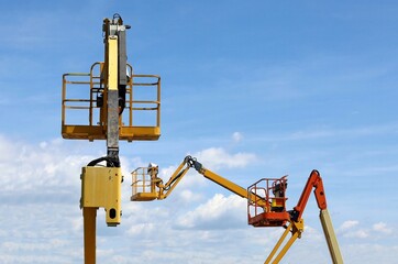 Aerial working platforms of cherry picker against blue sky with clouds. Back and side view, no people.