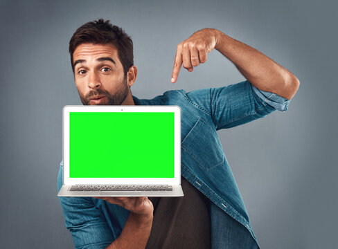 Man, Laptop And Pointing On Mockup Green Screen For Advertising Or Marketing Against A Grey Studio Background. Portrait Of Male Person Showing Computer Display, Chromakey Or Mock Up For Advertisement