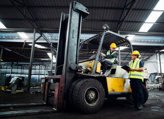 Industrial worker driving a forklift in the factory. Engineer is working and maintaining in the warehouse.