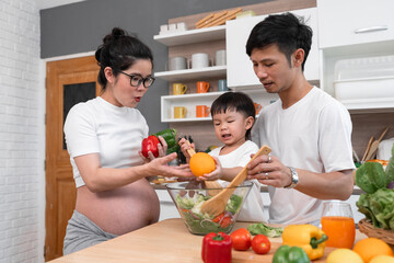 Asia pregnant mom cooking salad with father and son in kitchen at home