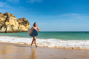 Fototapeta na wymiar Beautiful woman holding skimboard walking on sunny beach 